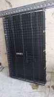 Full view of folded medium-sized black metal wire dog crate with double front doors, placed against a wall.