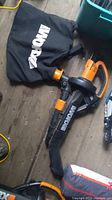 Side view of the Worx electric leaf blower with black collection bag bearing the Worx logo lying on wooden floor.
