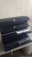 Four stacked black Sony PlayStation 3 consoles showing both slim and original models
