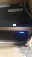 Front view of microwave powered on inside packaging showing digital control panel reading 12:00