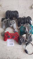 Five wired PlayStation controllers in various colors on white surface with cables coiled.