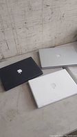 Three MacBook laptops closed on a flat surface showing black, white, and silver colors and Apple logos.