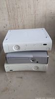Three Xbox 360 consoles stacked on top of each other on a surface. White, grey, and off-white colors visible.