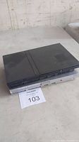 Two PlayStation 2 consoles stacked on a table, one black on top and one silver beneath, both untested.