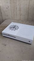 Front and top view of white Xbox One console with Assassin's Creed design on top surface.