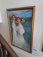 Framed painting on wall showing two women in white dresses and red hair against floral and cloudy background.