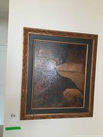 Framed abstract painting hung on a white wall, showing a dark textured artwork with a hand-like shape and ornate wooden frame.