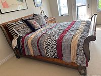 Full view of the queen size wooden sleigh bed made of wood with carved details, dressed with multi-patterned striped bedding and pillows.