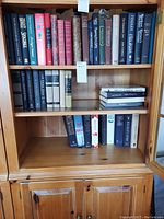 Wide view of three shelves in a wooden bookcase filled with mostly hardcover books in various colors and conditions.