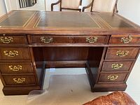 Photo of wood desk front, showing leather top with gold trim, multiple drawers with brass handles.