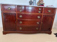 Front view of a wood dresser with stone top, showing three curved central drawers, two side cabinet doors, and drawer handles.