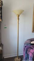 Full view of the gold floor lamp with glass shade, showing the base, pole, and top glass shade in an upright position near a couch.