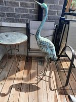 Front angle view of the metal bird figurine on an outdoor wooden deck near patio furniture.