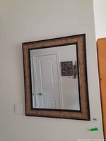Front view of the framed wall mirror hanging on a wall beside a door and a light switch.