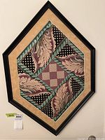 Front view of the framed needlepoint artwork showing detailed geometric and floral needlepoint design with cushioned mat and black frame.