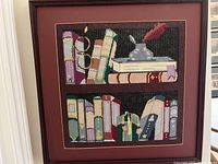 Front view of the framed needlepoint showing books and glasses design