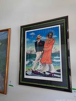Framed print hung on a wall showing a man and woman walking by the ocean, with clear details of the artwork and frame.