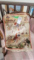 Photo of vintage Turkish rug showing colorful horsemen figures, floral patterns, and animals on a beige background with white fringes at the bottom.