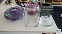 Top view of the lot showing the purple round glass dish, clear square vase, purple vase, tin kleenex holder, and clear round dish