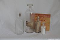 Set of four antique glass apothecary bottles and antique drug store advertisement card arranged on white background.