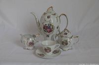 Full set showing teapot, creamer, sugar bowl, teacup and saucer with hand-painted garden motif and gold accents