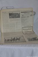 Photo of an open newspaper showing text, advertisements, and black and white photos including horse racing imagery.