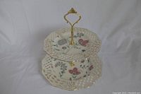 Front view of two tier ceramic cake tray showing floral designs and gold lattice edges.