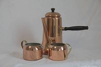 Front view of vintage copper coffee or tea pot with creamer and sugar bowl on either side