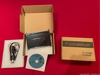 Two 7-inch LCD screens in boxes with cables and driver CDs, showing front screen and packaging.