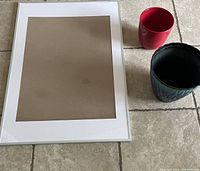 IKEA Lomviken 24.5x36.5 silver frame laid flat beside two ceramic pots: one red, one blue.