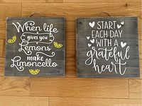 Two square handmade wooden wall hangings featuring inspirational quotes with lemon and heart accents on a natural wood floor.