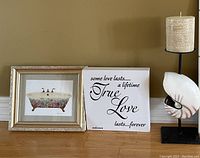 Two pieces of wall art positioned on floor against wall, one framed print and one canvas with quote.