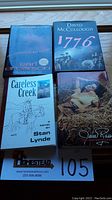 Four books laid out on wooden surface with visible covers: 'Careless Creek' light blue cover, '1776' blue cover, 'Jane Russell An Autobiography' photographic cover, and 'The Million Dollar Tattoo' black cover.