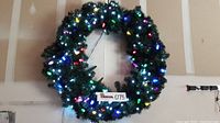 Large lighted evergreen wreath displaying multi-colored lights, approx. 40 inches diameter hung on wall