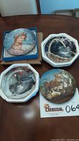 Four collector plates laid out on a wooden table showing scenes of mother with child, cats, and lion cubs