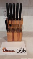 Set of six black-handled Fiskars knives, knife sharpener, and wooden block arranged with knives and sharpener inserted into the slots of the block.