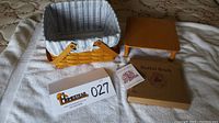 Photo of the handwoven basket with fabric liner and plastic insert, wooden basket stand, boxed warming brick, and booklet on a soft white surface.
