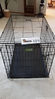 Full view of black metal pet crate with plastic floor tray inside, shown on carpeted floor.