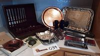 Full view of the lot showing flatware box, metal trays, wooden bowls, napkin rings, cutting utensils, and plaque on a countertop.
