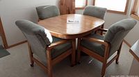 Four pale green upholstered rolling chairs around oak dining table with leaf extension.