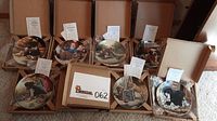 Photo showing 7 boxed collectible plates with information cards included, titles visible on cards.