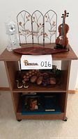 Wooden rolling cart with shelf displaying various decorative items such as a carved wooden fruit bowl, a vinyl figurine, a crystal clock, and a metal tea light holder.