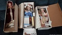 Three porcelain dolls in their original boxes on a couch, showing full set and packaging