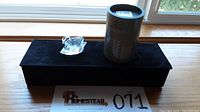 Photo showing the swan figurine on a black velvet cushion next to the original cylindrical Swarovski box and a numbered lot tag.