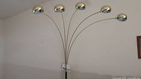 Full view of the tall brass floor lamp with five curved arms each topped with a polished dome shade.