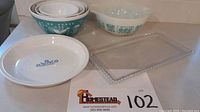 Five vintage glass kitchenware pieces including Pyrex Charm mixing bowls, white Corning bowl, and Candlewick glass platter.
