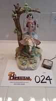 Front view of handpainted Arnart porcelain sculpture showing young couple on tree swing with certificate of authenticity placed beside it.