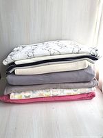 Stack of folded cotton knit fabrics in light colors including white with animal prints, gray, and pink.