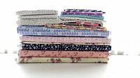 Stack of folded organic cotton fabrics showing a variety of patterns and colors including dots, animal shapes, and nature scenes
