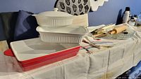 Photo showing ceramic baking and casserole dishes stacked together with heavy metal acorn mold pan in background and kitchen linens on the side.
